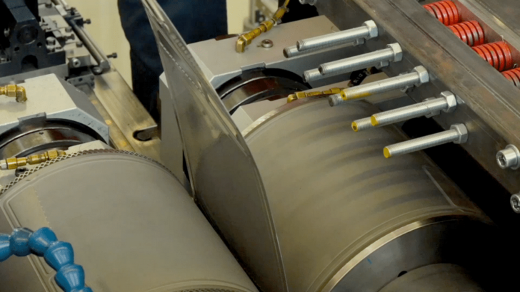 Close-up of industrial printing press rollers in operation, showing mechanical parts and metal components. Close-up of industrial printing press rollers in operation, showing mechanical parts and metal components.