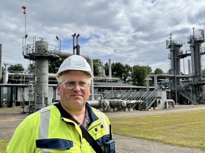 Man in safety gear and hard hat stands in front of industrial facility with pipes and tanks outdoors. Man in safety gear and hard hat stands in front of industrial facility with pipes and tanks outdoors.